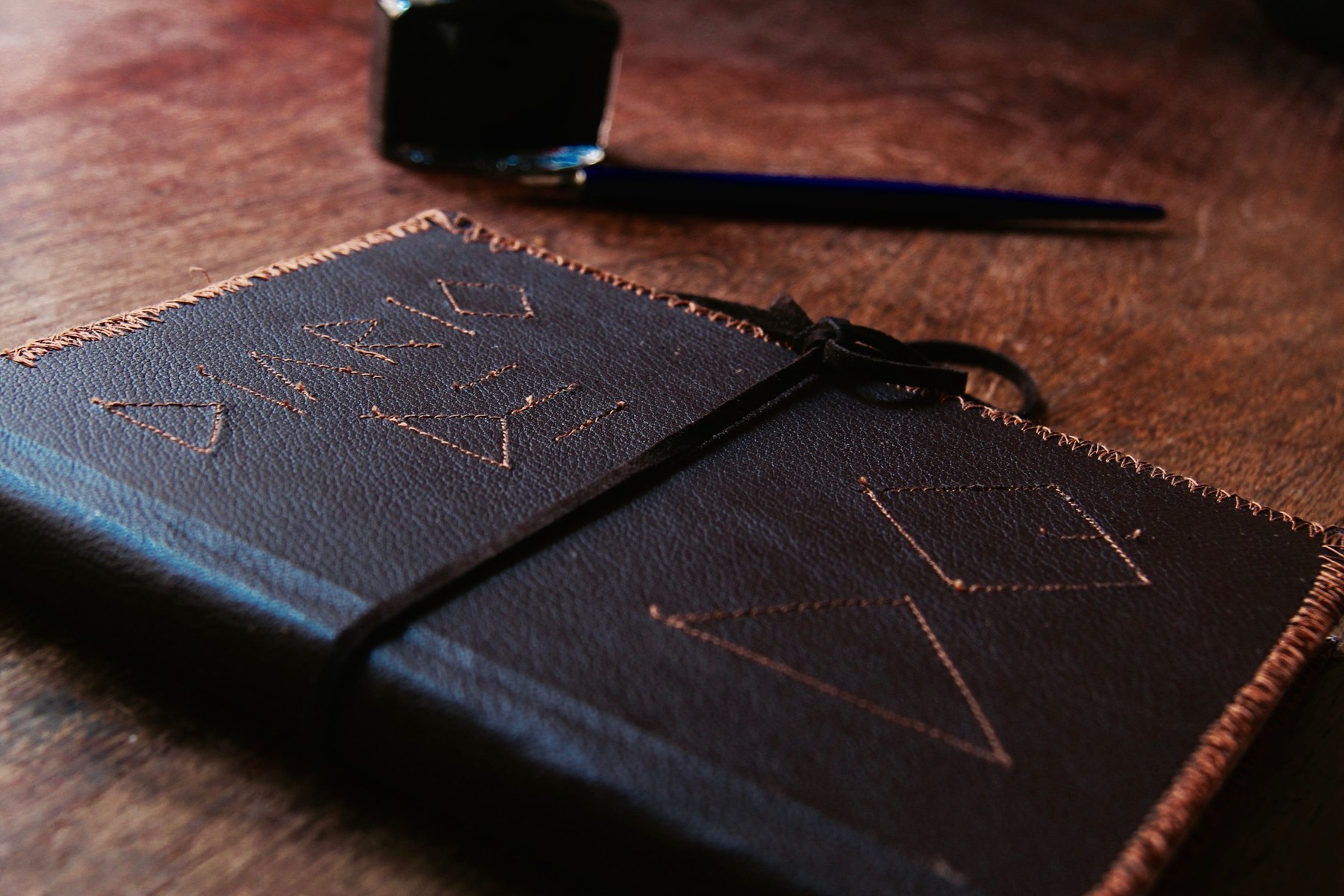 A leather-bound diary, an inkwell and a dip pen on a wooden table
